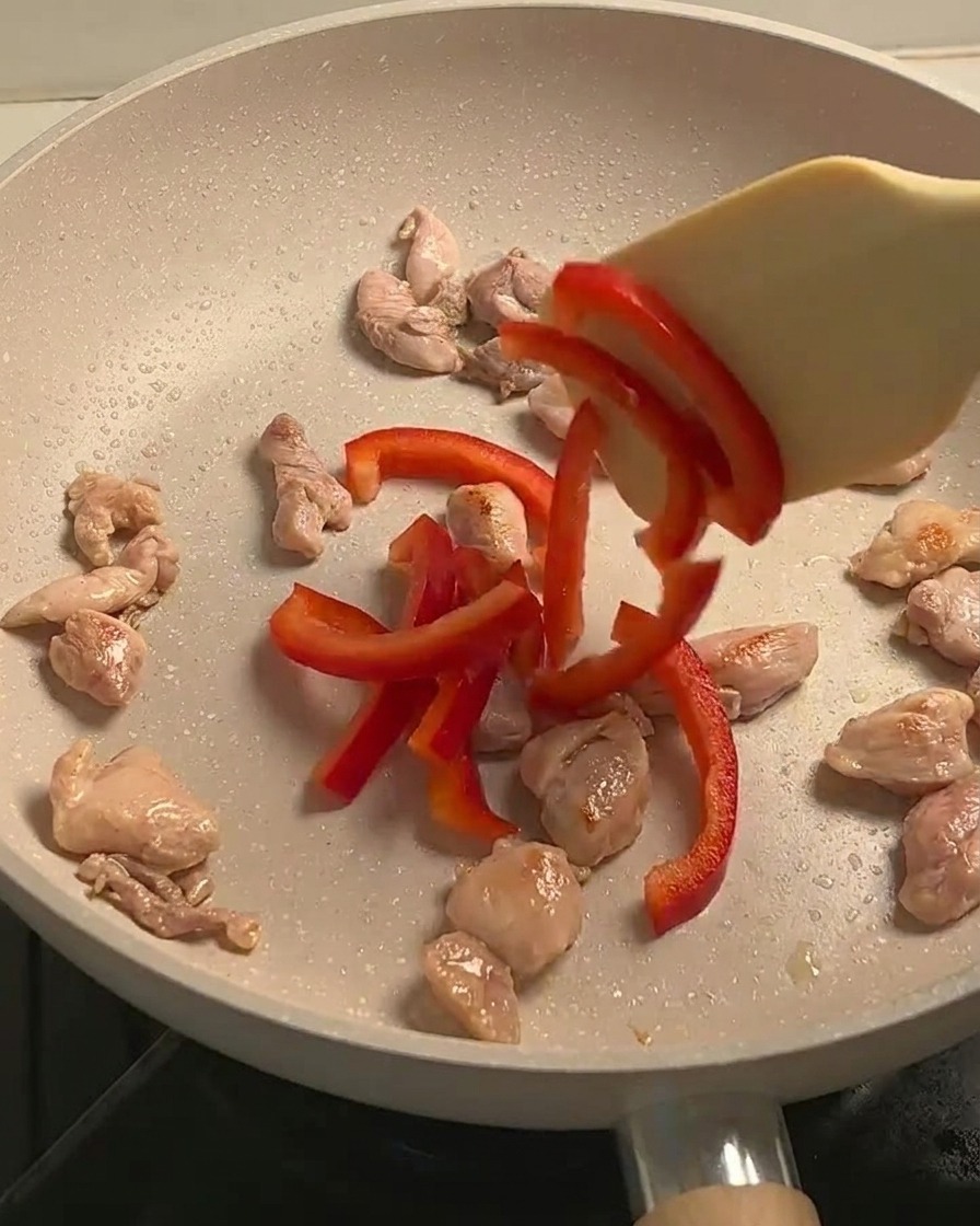 Poulet sauté, lamelles de poivrons rouges et champignons cuisant ensemble dans une poêle.