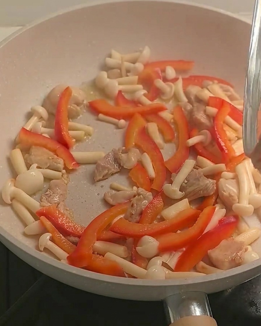 Fusilli cuits ajoutés dans la poêle contenant le mélange de poulet et de légumes colorés.