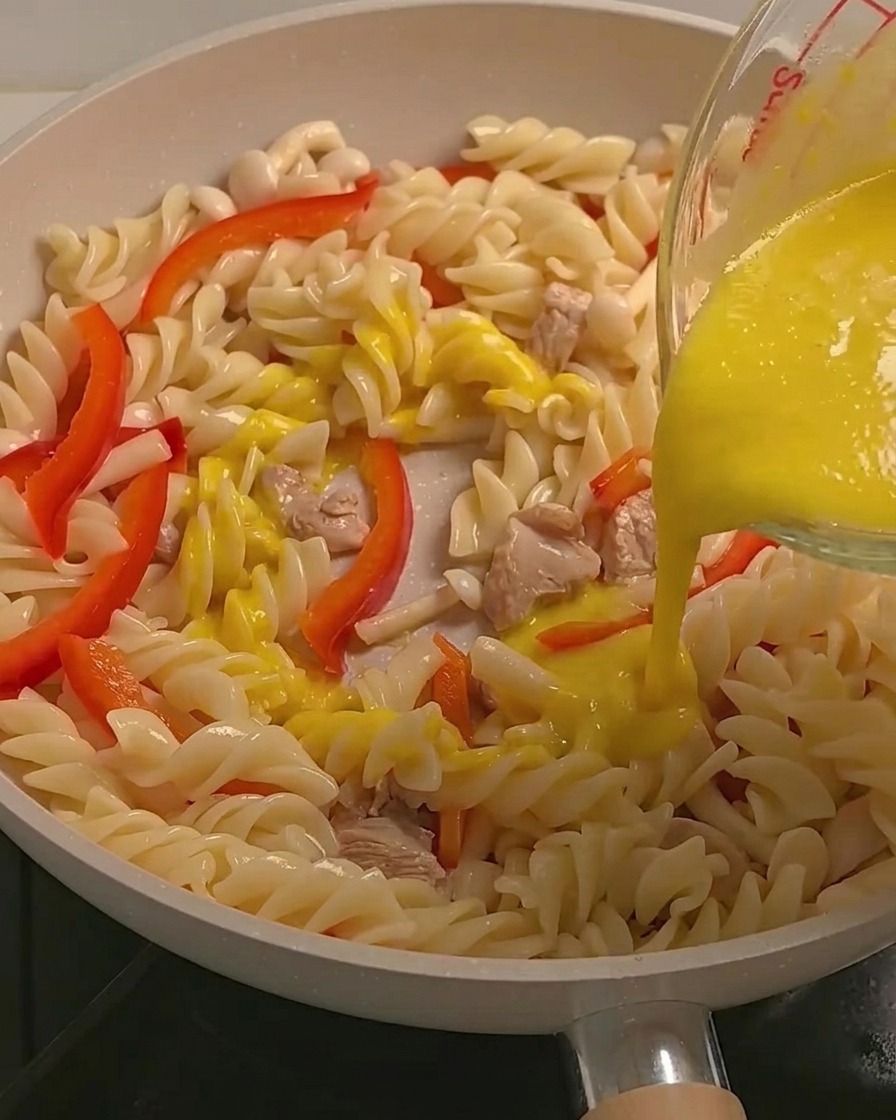 Sauce crémeuse jaune au potiron versée sur les fusilli, le poulet et les légumes dans une poêle.