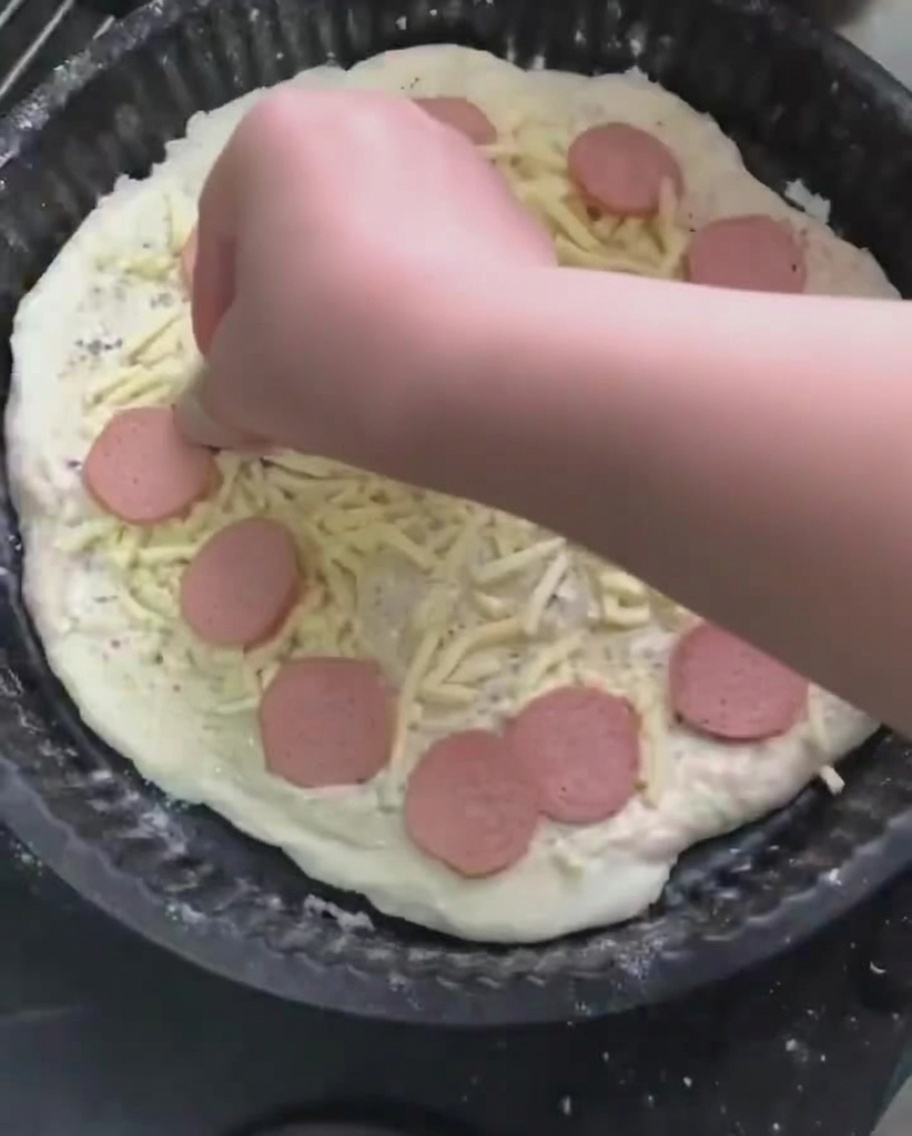 Rondelles de saucisse posées sur le lit de mozzarella râpée de la pizza.