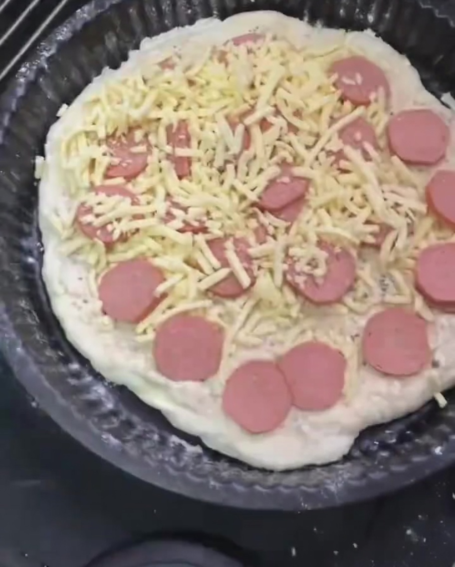 Une dernière couche généreuse de mozzarella râpée étalée sur la pizza garnie de saucisses.