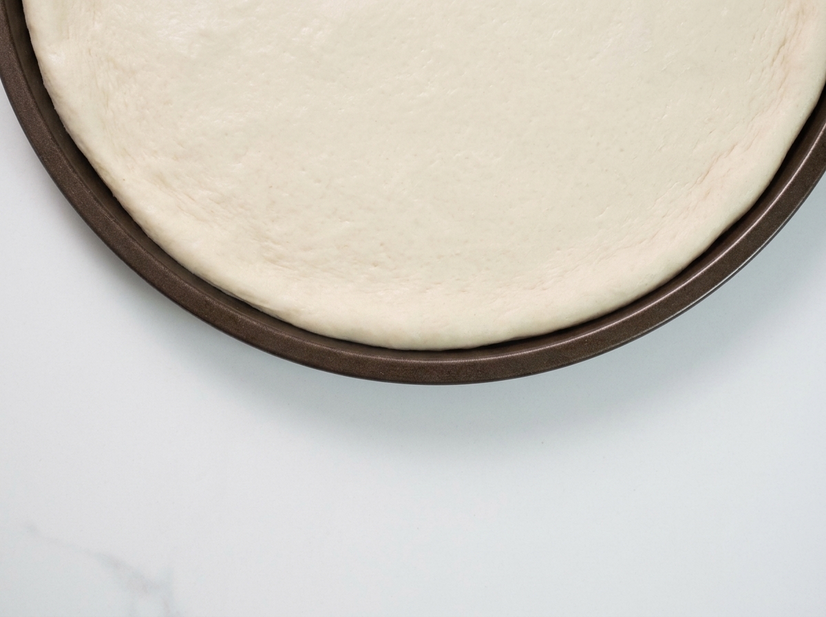 Une cuillerée de sauce à la truffe noire étalée sur une base de pâte à pizza crue.