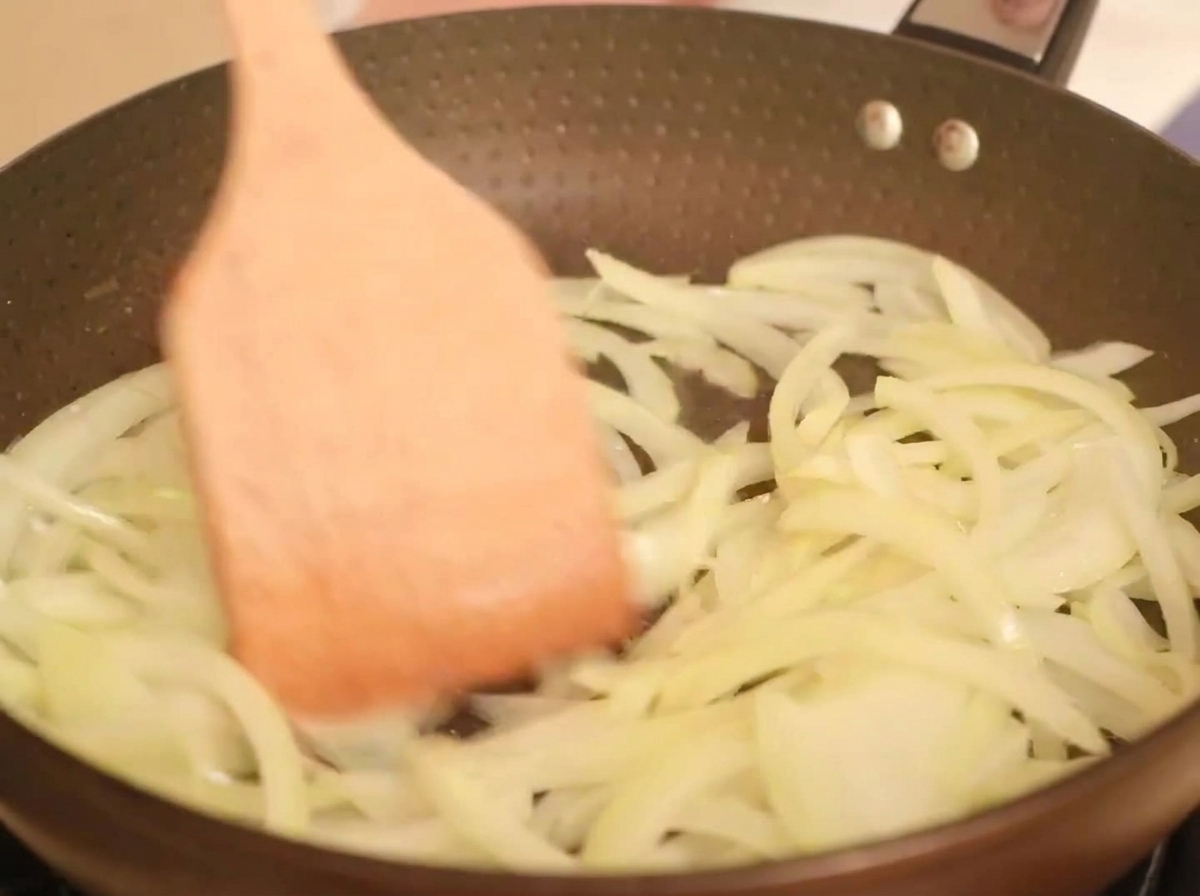 Lamelles doignon jaune cuisant dans une poêle chaude avec de lhuile, remuées avec une spatule en bois.