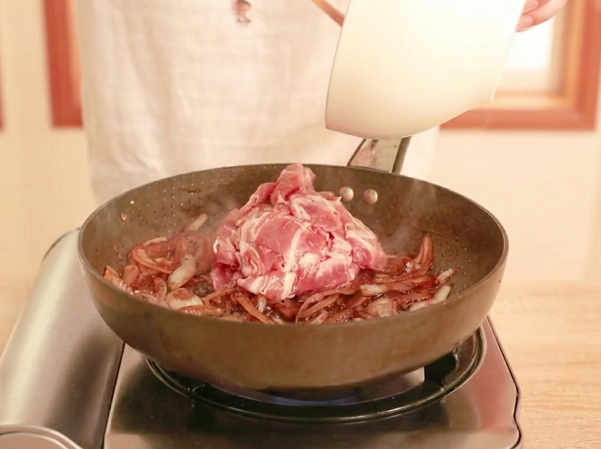 Bœuf cru finement tranché ajouté dans une poêle avec une sauce foncée et des oignons ramollis, prêt à être sauté.