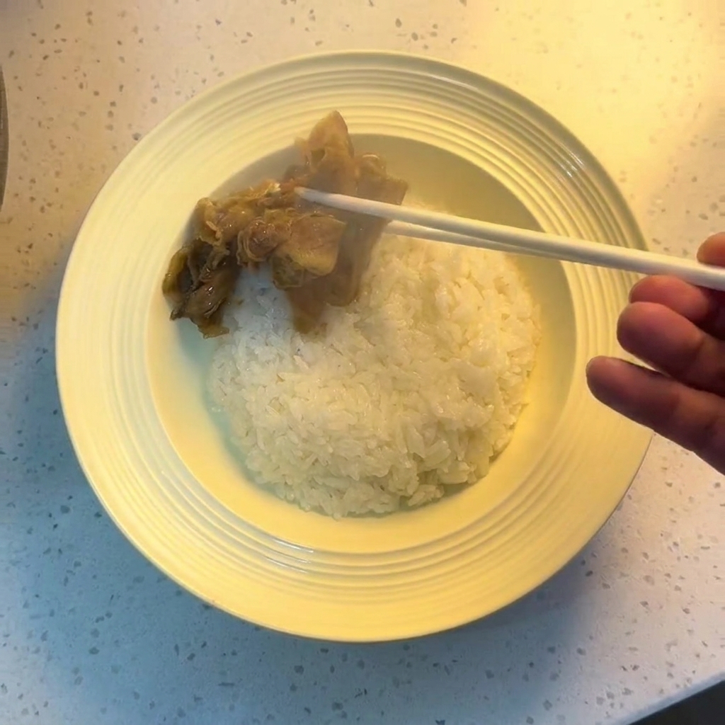 Baguettes déposant le bœuf et les oignons cuits sur un bol de riz blanc.