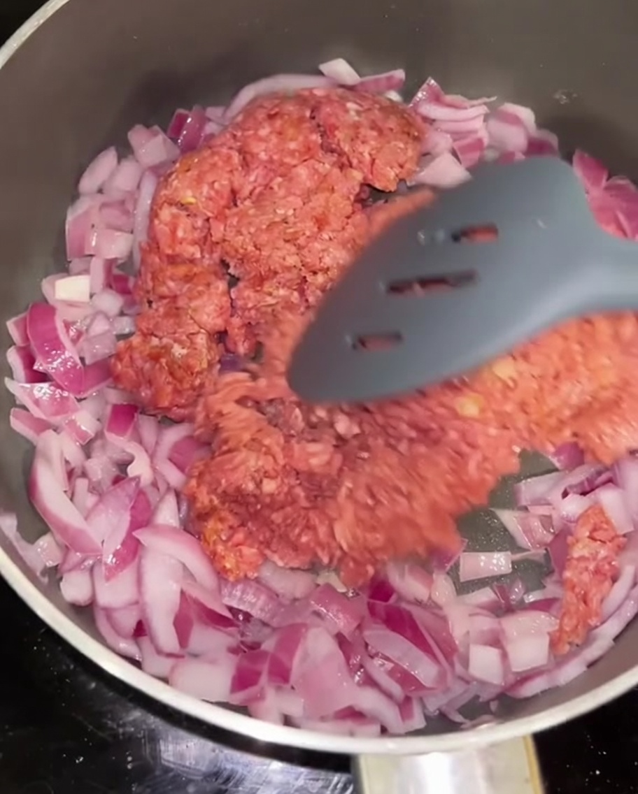 Bœuf haché en train dêtre sauté avec de loignon rouge dans une poêle.