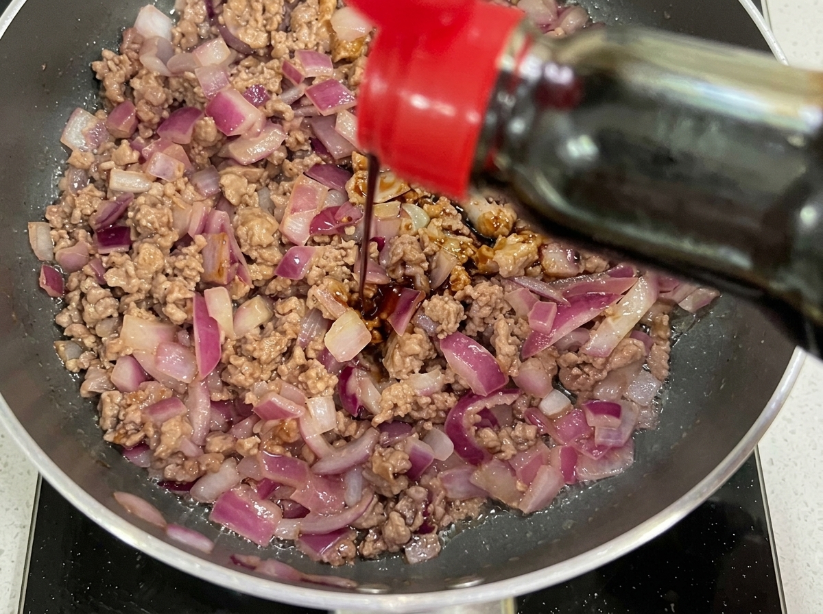 Sauce soja foncée et ketchup ajoutés à la poêle de bœuf et doignons sautés.