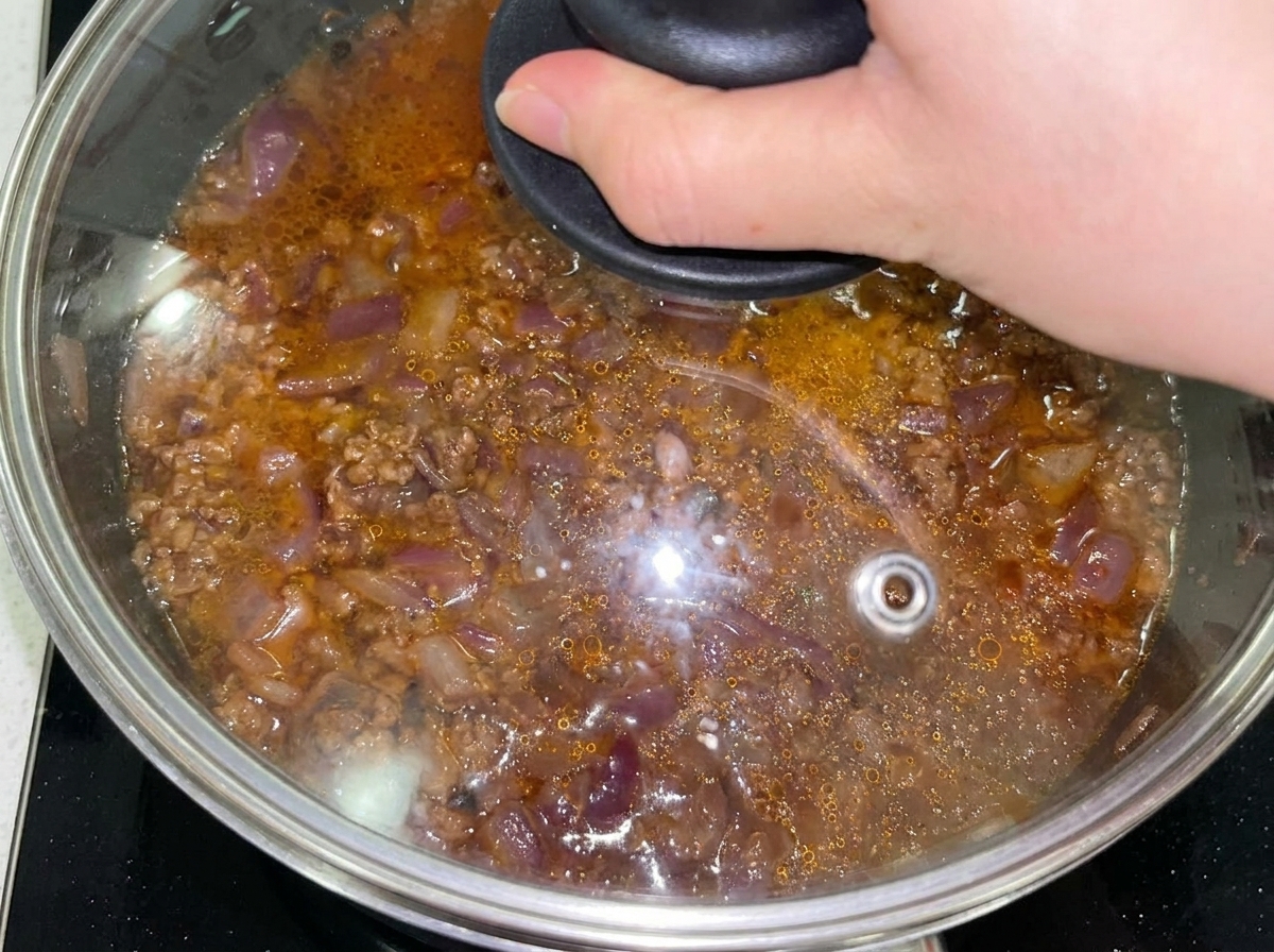 Mélange de bœuf et doignons dans une poêle couverte après lajout deau.