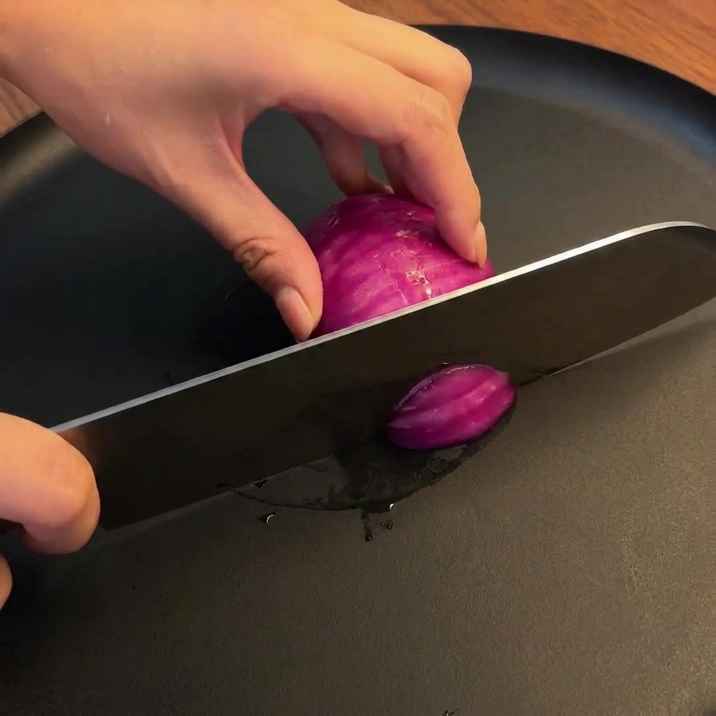 Un oignon rouge tranché en morceaux épais et uniformes sur une planche à découper en bois avec un couteau de chef.