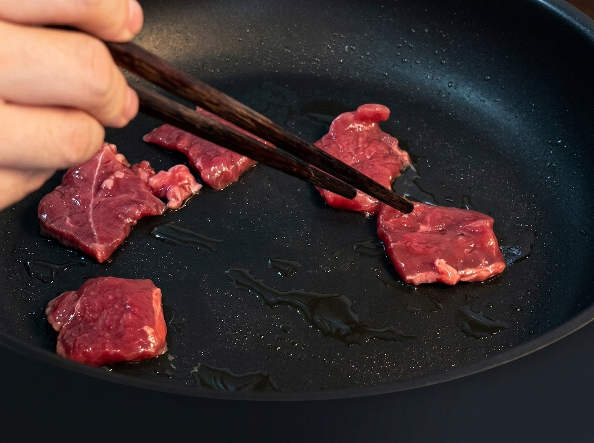 Fines tranches de bœuf en train de dorer dans une poêle chaude huilée.