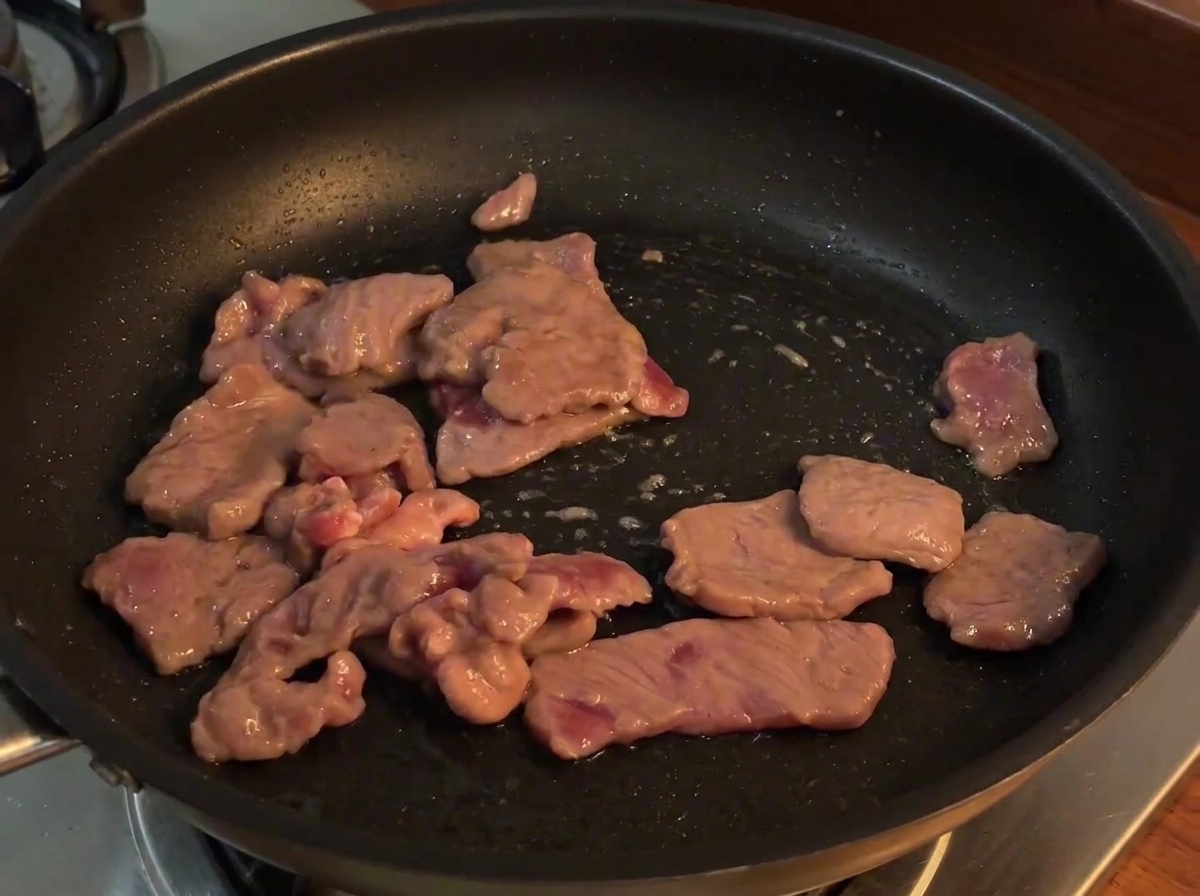 Tranches doignon rouge ajoutées dans la poêle avec le bœuf cuit, en train dêtre mélangées à la chaleur.