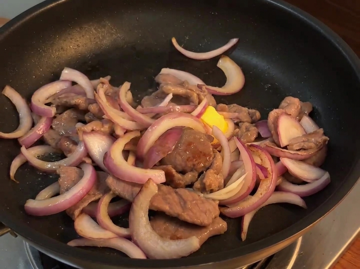 Sauce sautée versée dun petit bol sur le mélange bœuf et oignon dans une poêle chaude.