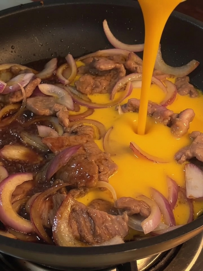Gros plan sur les œufs battus versés dans une poêle sur le bœuf et les oignons sautés.