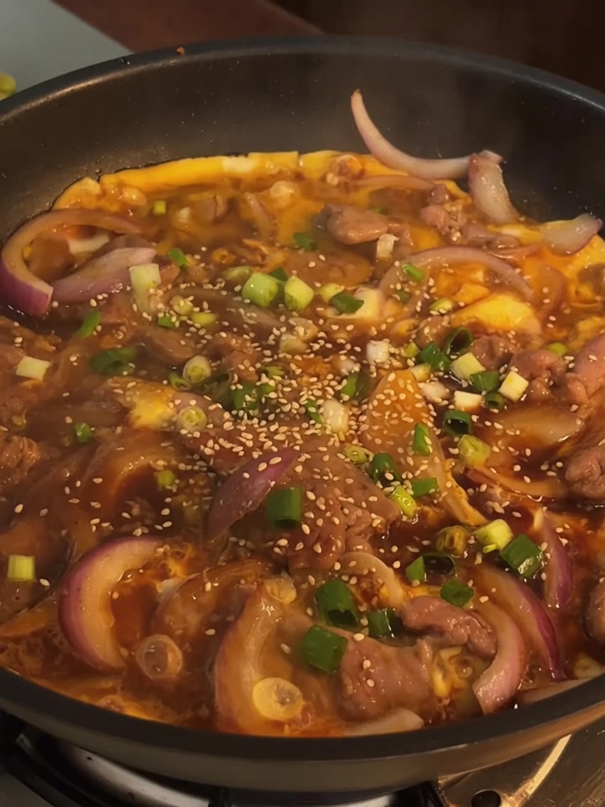 Plat de bœuf et œuf fini dans une poêle, garni doignons verts frais hachés et de graines de sésame grillées.