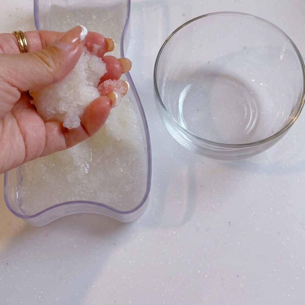 Une main pressant leau hors du radis daikon râpé à côté dun bol en verre transparent.