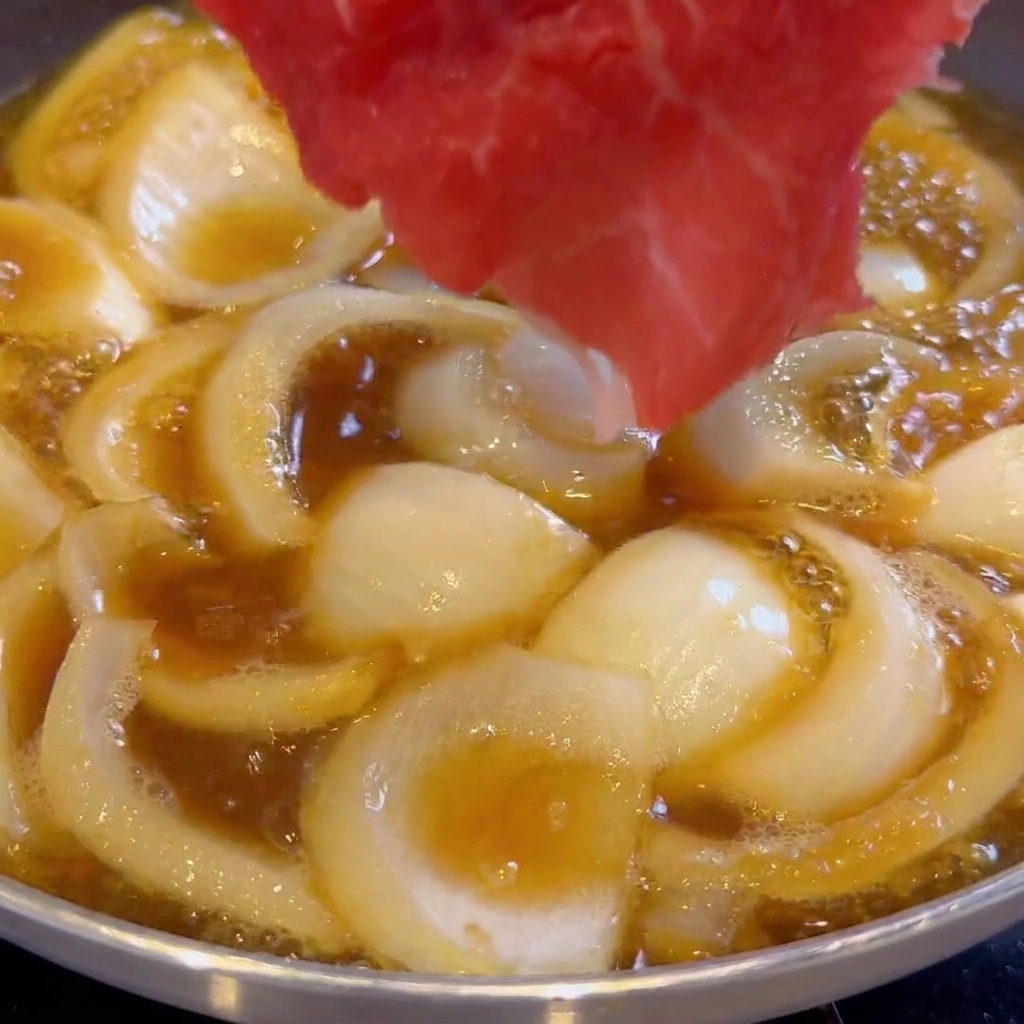De fines tranches de bœuf cru déposées dans une poêle avec les oignons et la sauce.