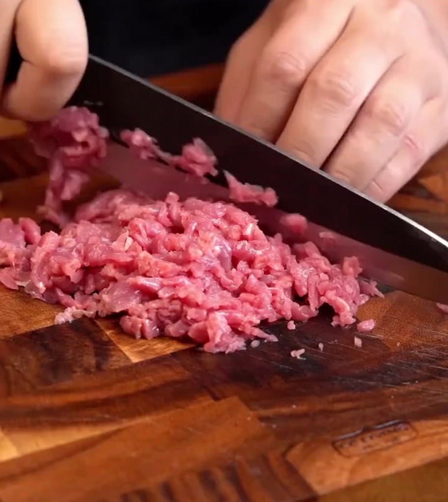 Pâte de bœuf frais finement hachée sur une planche à découper en bois, prête à être assaisonnée.
