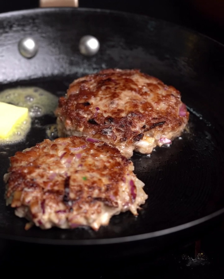 Steaks de bœuf friant dans une poêle avec un morceau de beurre fondant et une branche de romarin frais.