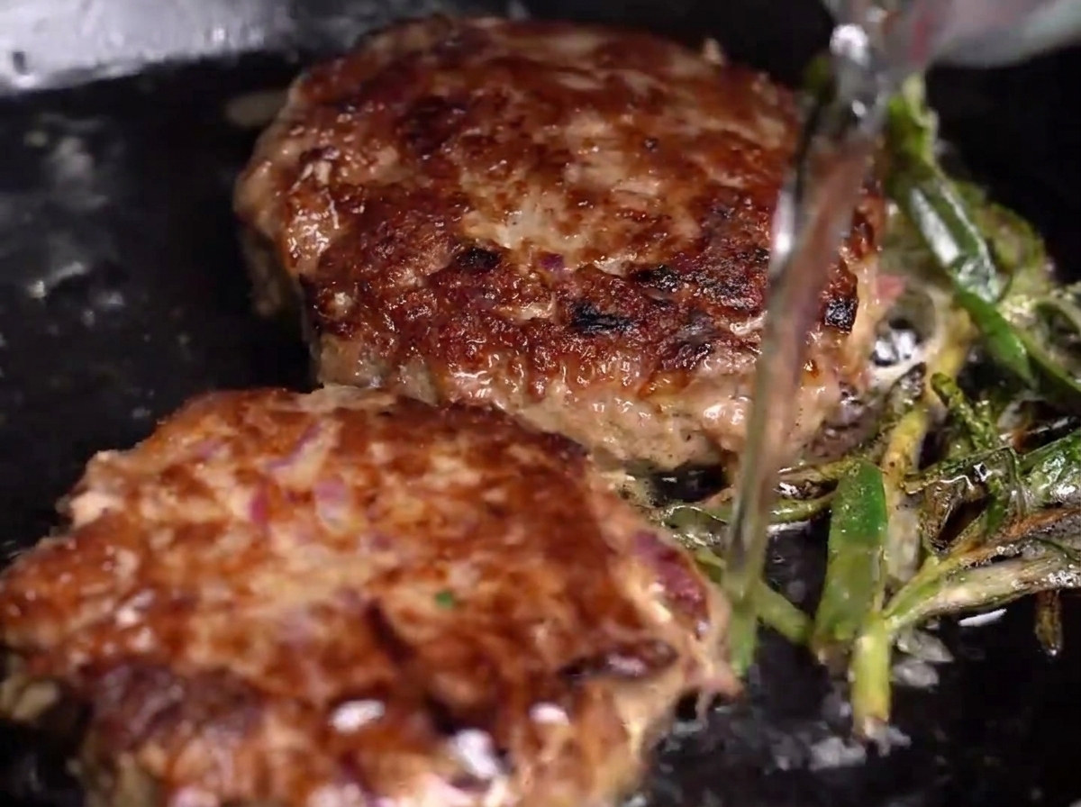 Ajout dun peu deau dans une poêle chaude contenant les steaks et les herbes, générant de la vapeur.