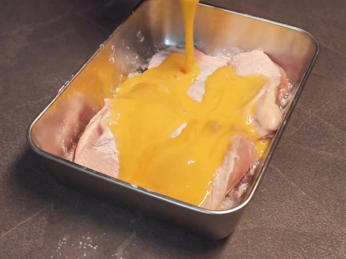 Cuisse de poulet enrobée de fécule plongée dans un récipient rempli dœuf battu doré.