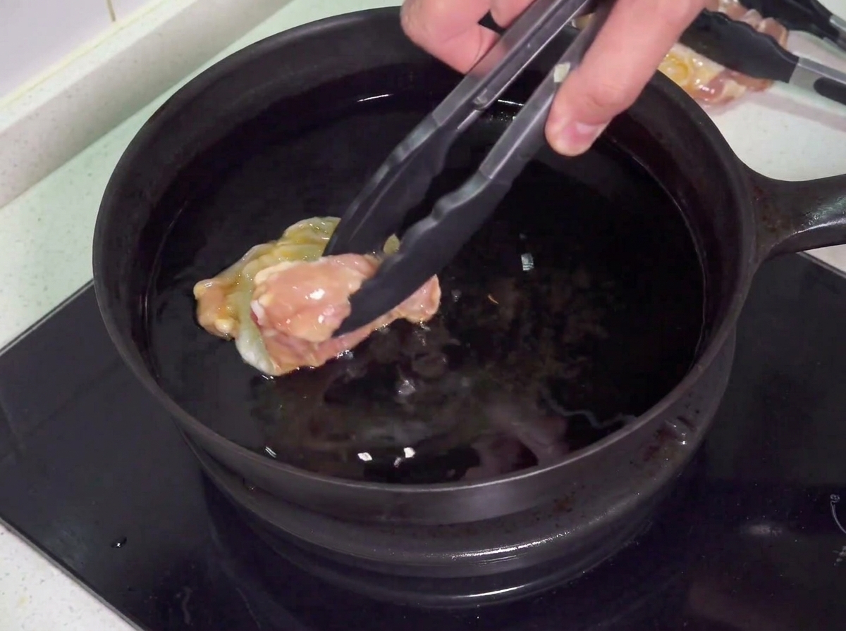 Cuisses de poulet crues délicatement déposées dans une poêle remplie dhuile chaude pour la friture.