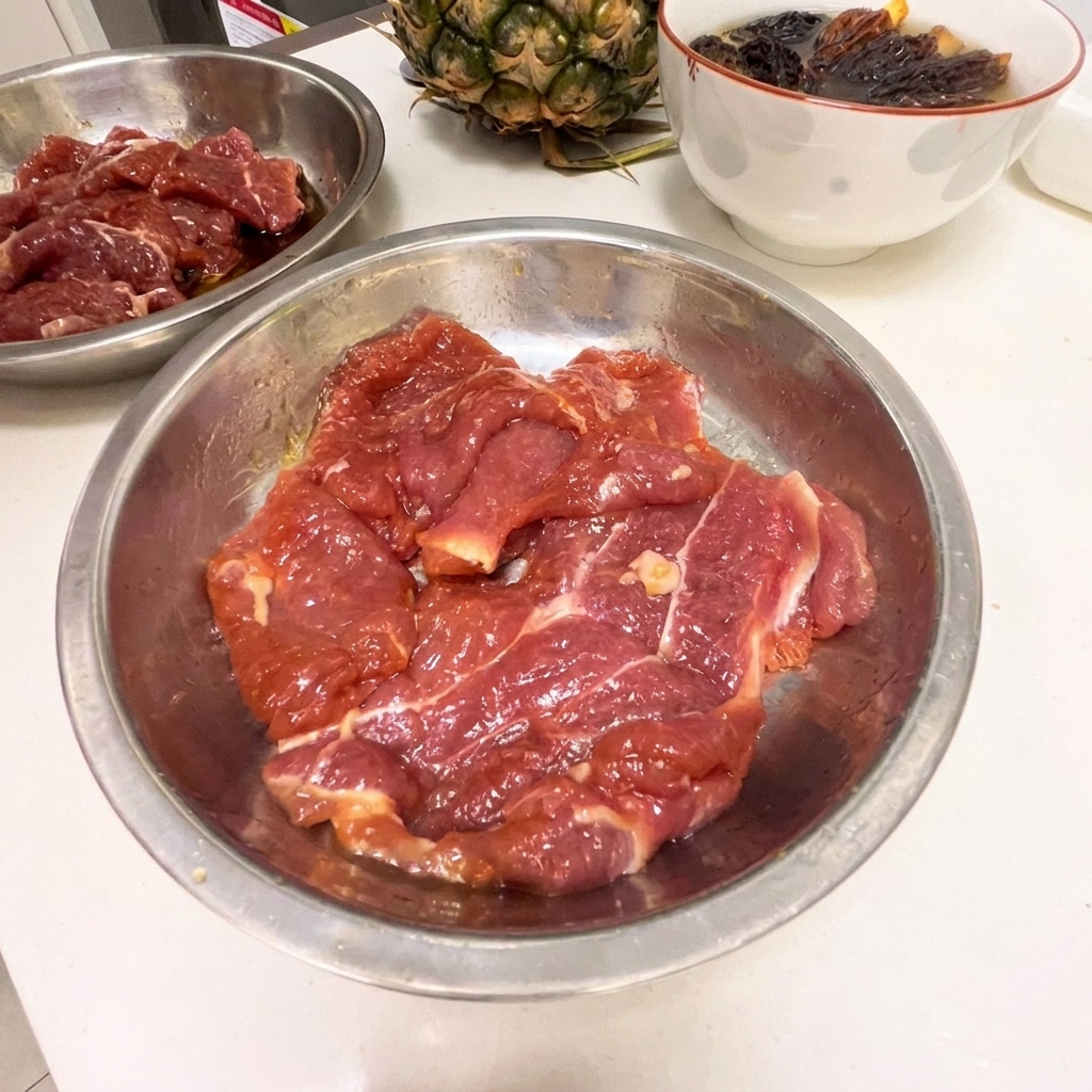 Fines tranches dépaule de porc crue dans un bol en inox avec la marinade sombre.