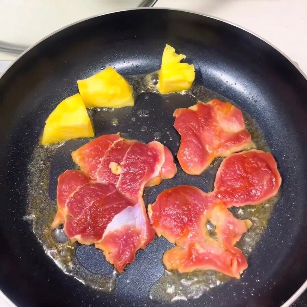 Tranches de porc cru et morceaux dananas jaune cuisant dans une poêle avec de lhuile.