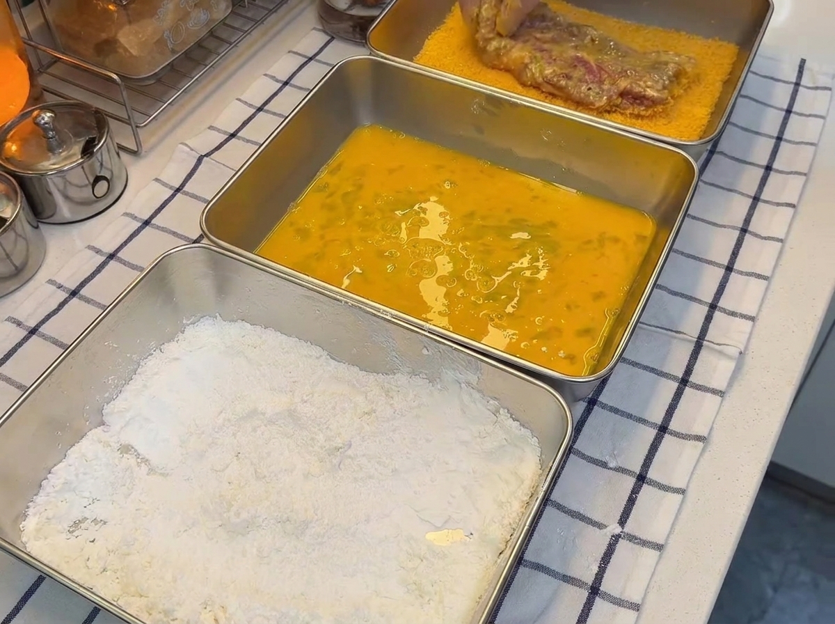 Un morceau de porc fermement pressé dans un plateau en métal rempli de chapelure dorée.
