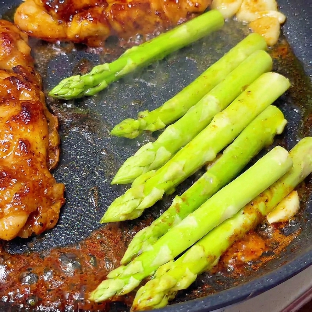 Asperges vertes fraîches mijotant à côté des blancs de poulet glacés dans une poêle.
