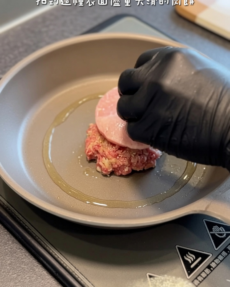 Un steak haché cru délicatement déposé dans une poêle chaude huilée à laide dune main gantée et dune spatule.