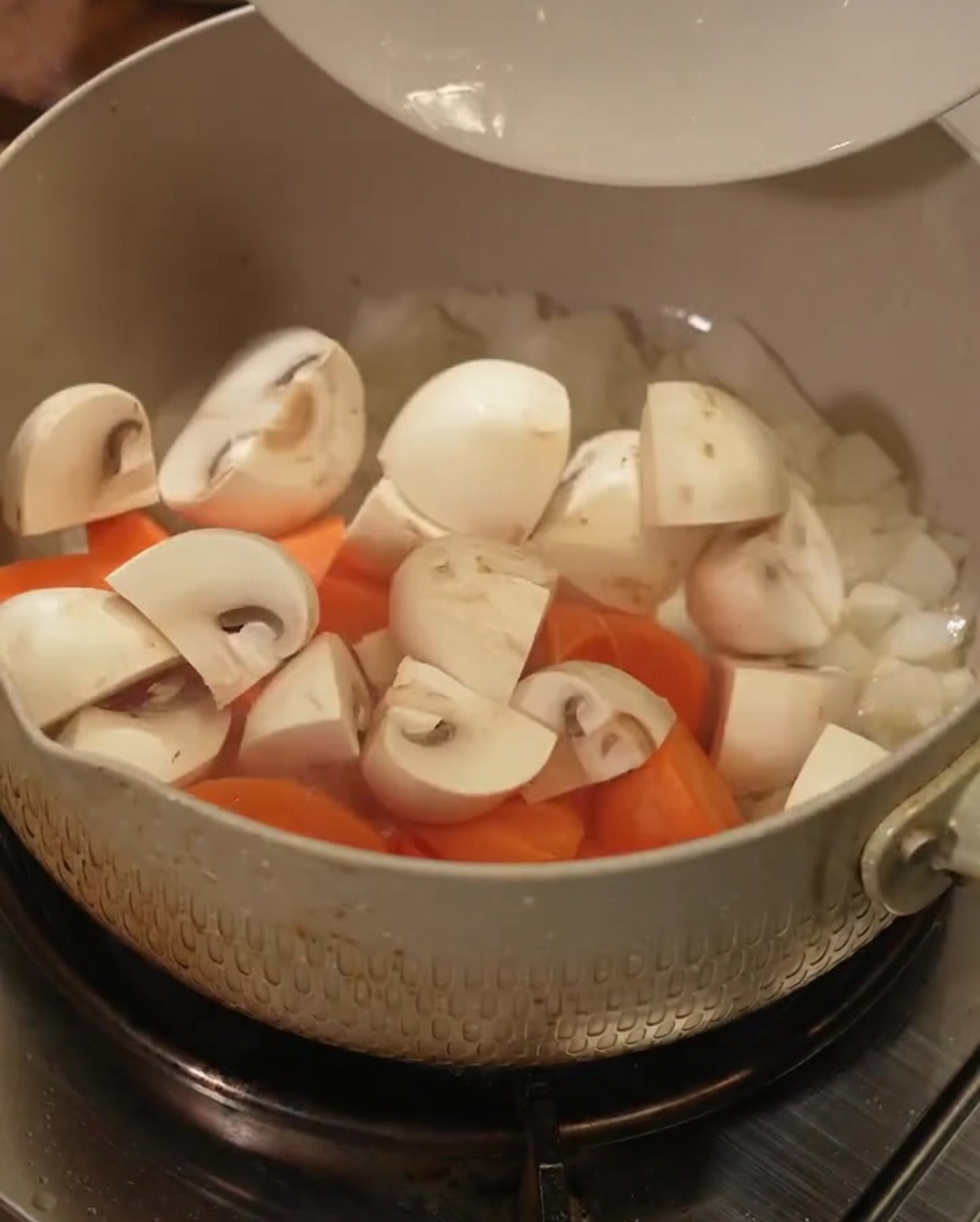 Des morceaux de carottes frais et des tranches de champignons jetés dans une casserole.