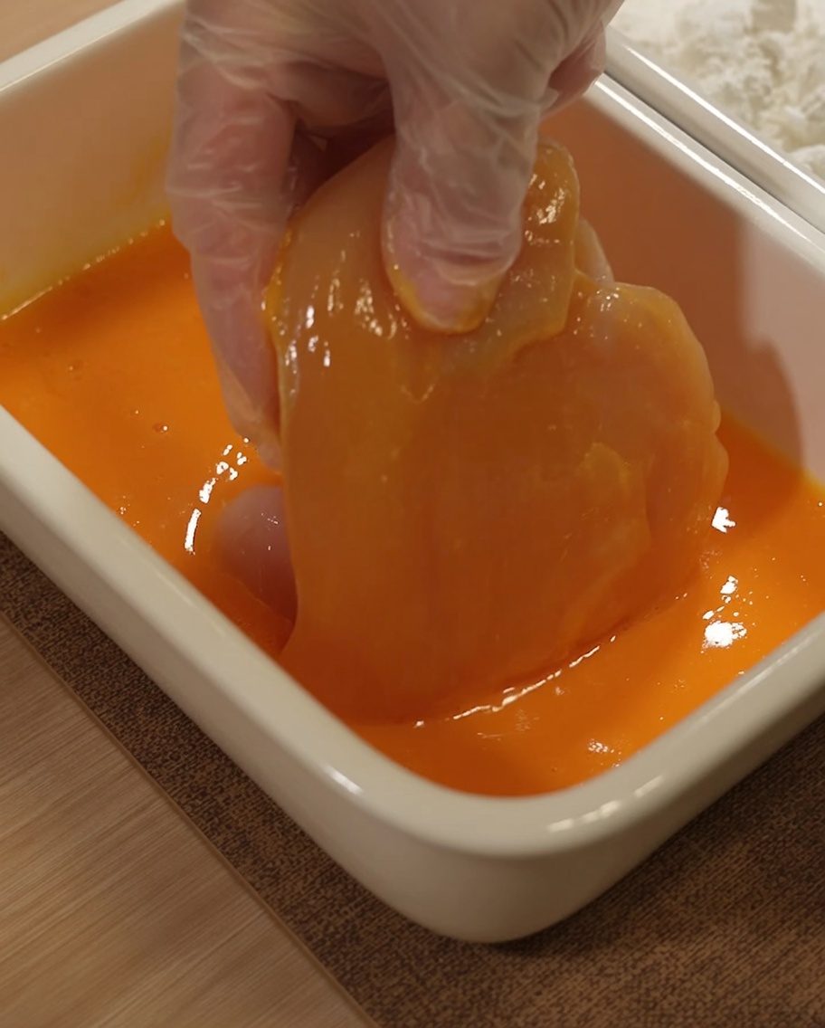 Un blanc de poulet immergé dans un mélange dœuf battu jaune.
