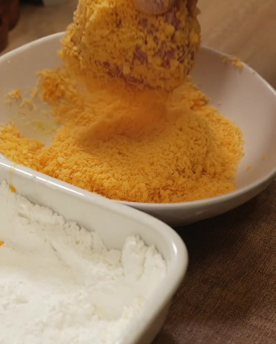 Un blanc de poulet pressé fermement dans un bol de chapelure dorée pour un enrobage uniforme.