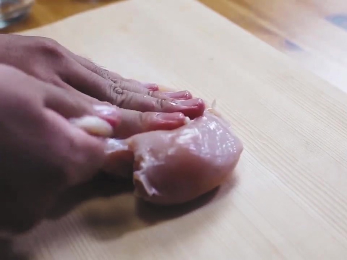 Un blanc de poulet cru saupoudré de sel sur une planche à découper en bois.