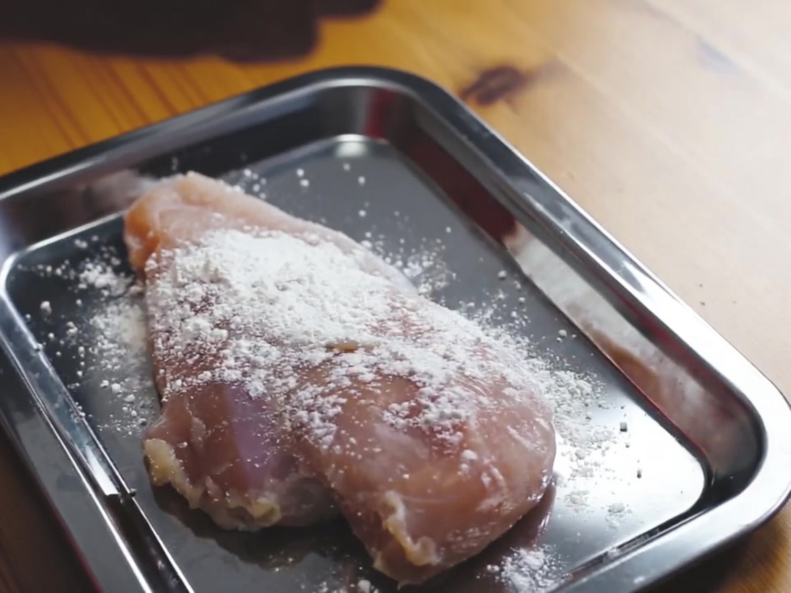 Un blanc de poulet enrobé de farine sur un plateau métallique.