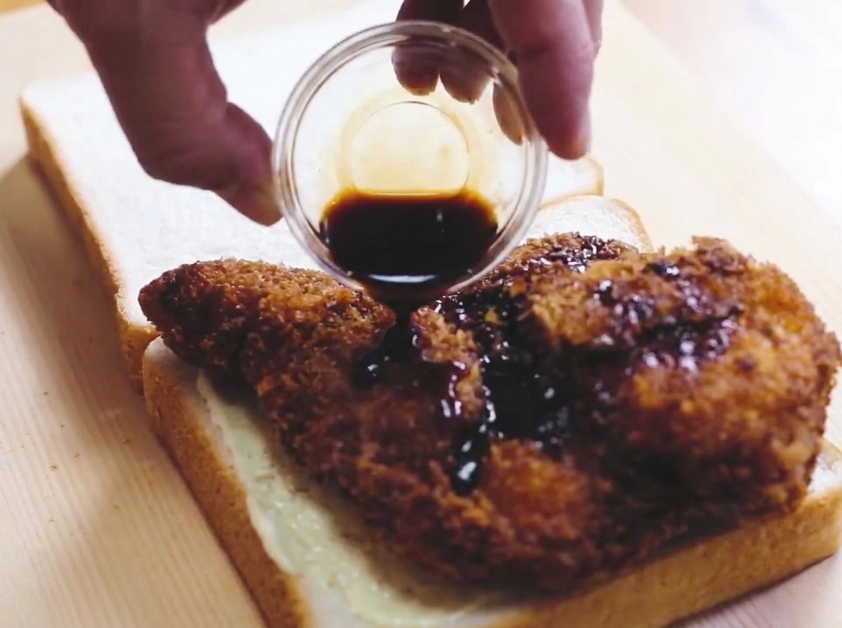 Le poulet frit posé sur une tranche de pain et nappé de sauce.