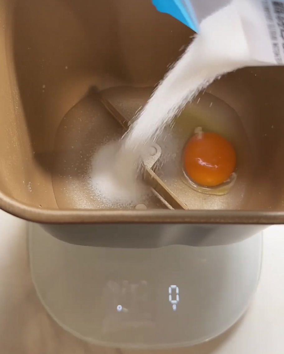 Les ingrédients pour la pâte à pain, incluant lœuf et le sucre, versés dans la cuve de la machine à pain.