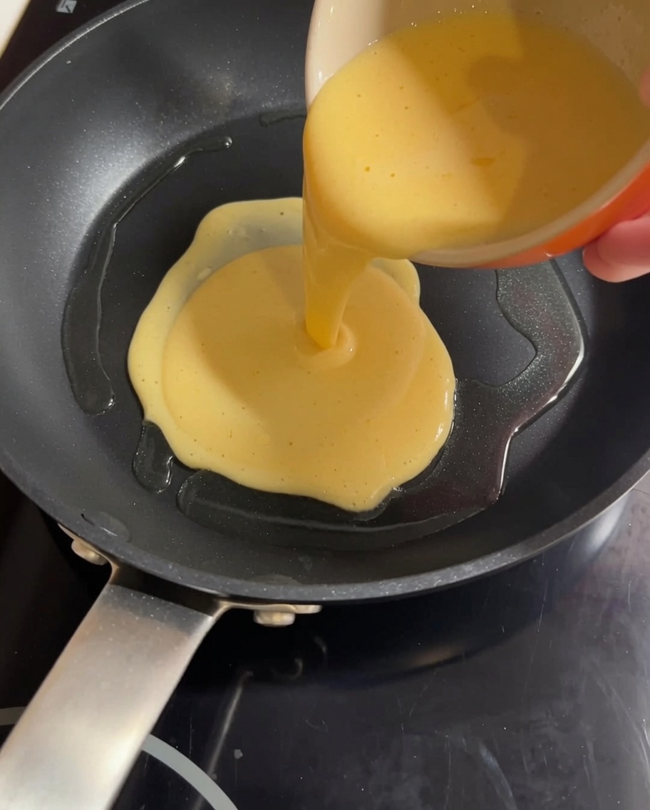 Un mélange jaune dœuf et de lait versé dans une poêle chaude, prêt à être brouillé.
