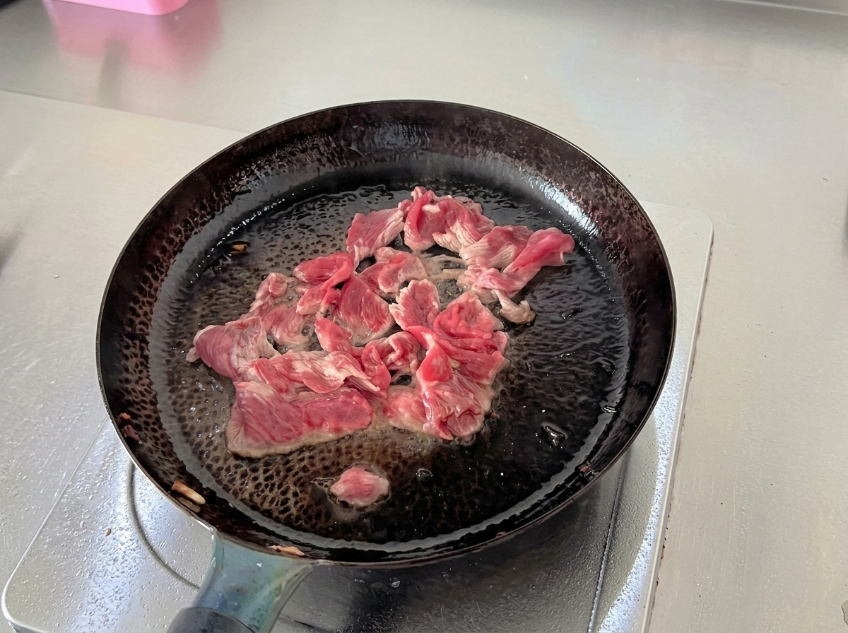 De fines tranches de bœuf cru rouge ajoutées dans une poêle chaude.