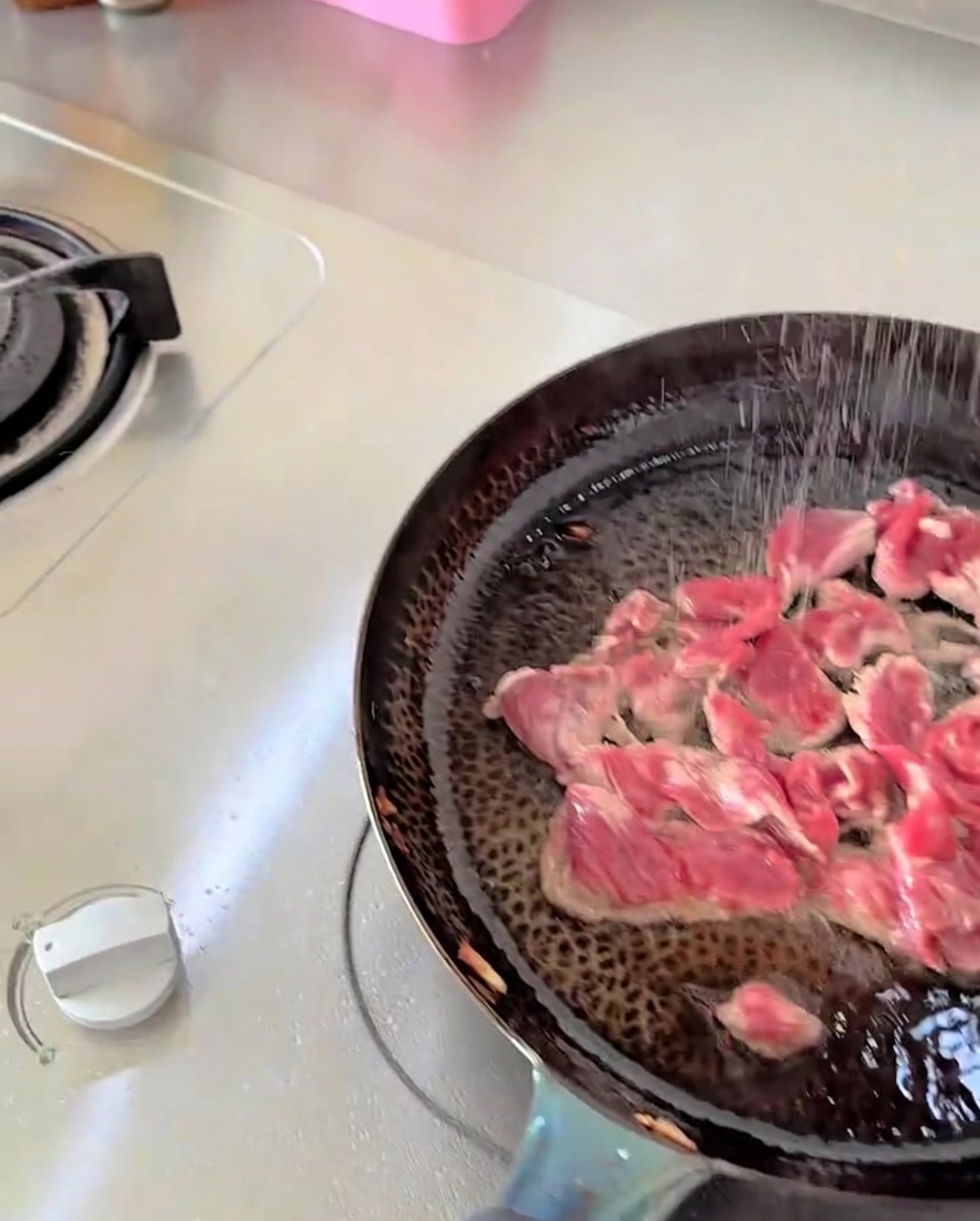 Du sel et des assaisonnements saupoudrés den haut sur du bœuf tranché cuisant dans une poêle.