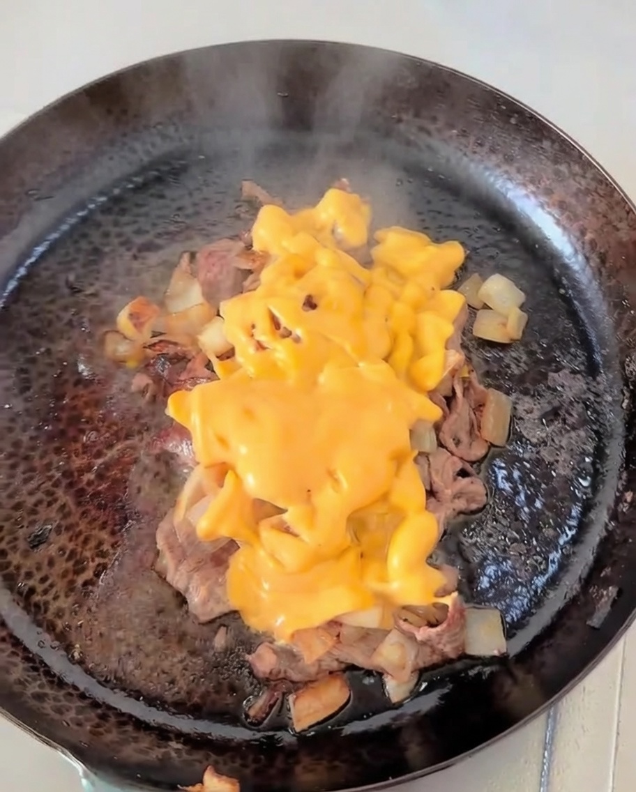 Une spatule mélangeant du fromage fondu dans une poêle avec du bœuf doré et des oignons caramélisés.