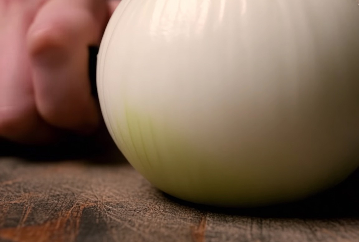 Un oignon blanc coupé en fines lamelles sur une planche à découper.