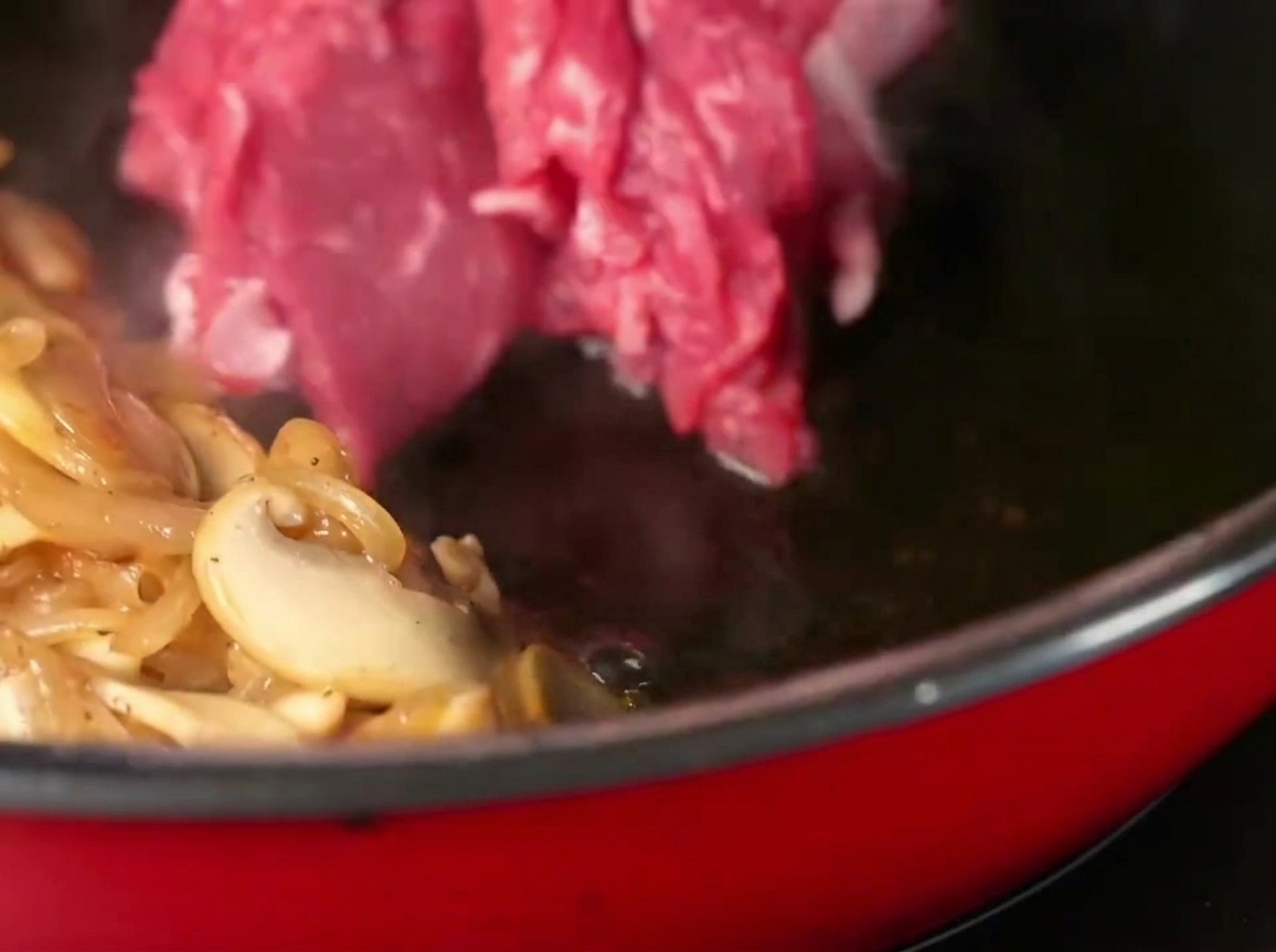 Lamelles de faux-filet ajoutées à la poêle avec les légumes, assaisonnées de sel et de poivre.