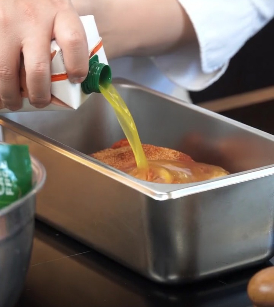 Du jus dorange versé dune brique dans un plat de cuisson contenant le porc assaisonné.