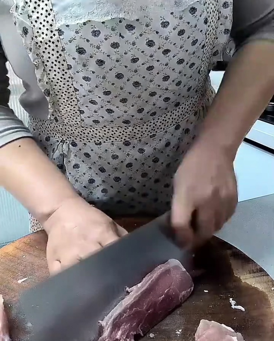 Un couperet tranchant coupant des morceaux de porc maigre sur une planche à découper en bois.