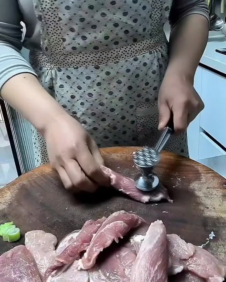 Un maillet à viande attendrissant de fines tranches de porc cru sur une surface en bois.