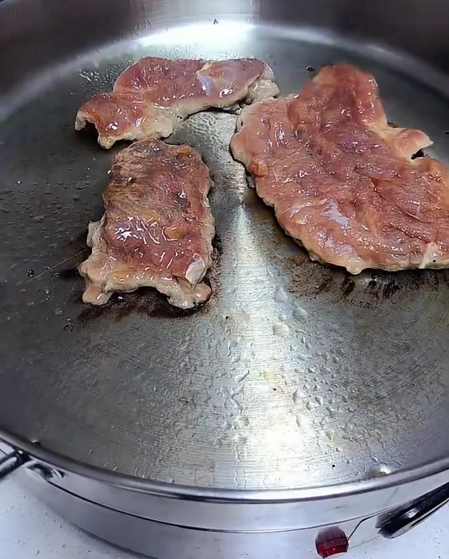 Des côtes de porc marinées saisies dans une poêle chaude, avec un brunissement visible sur la surface.
