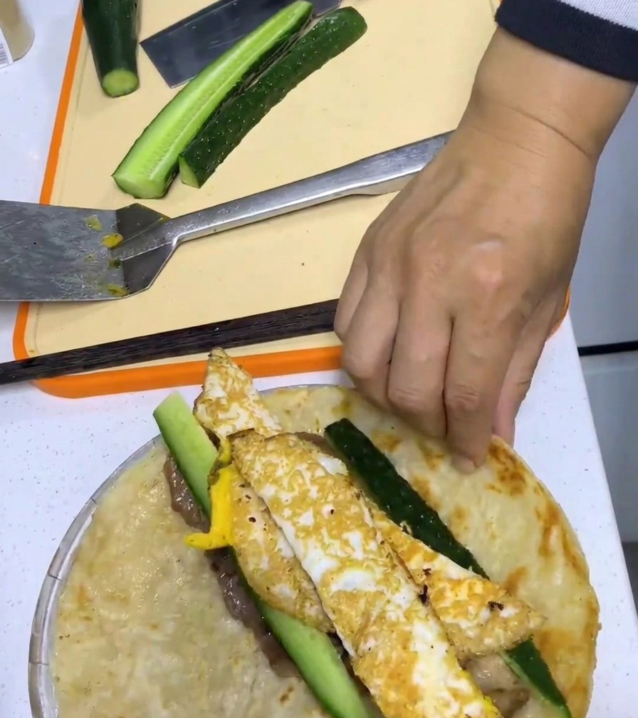 Une main roulant étroitement le pancake autour du porc, de lœuf et du concombre.