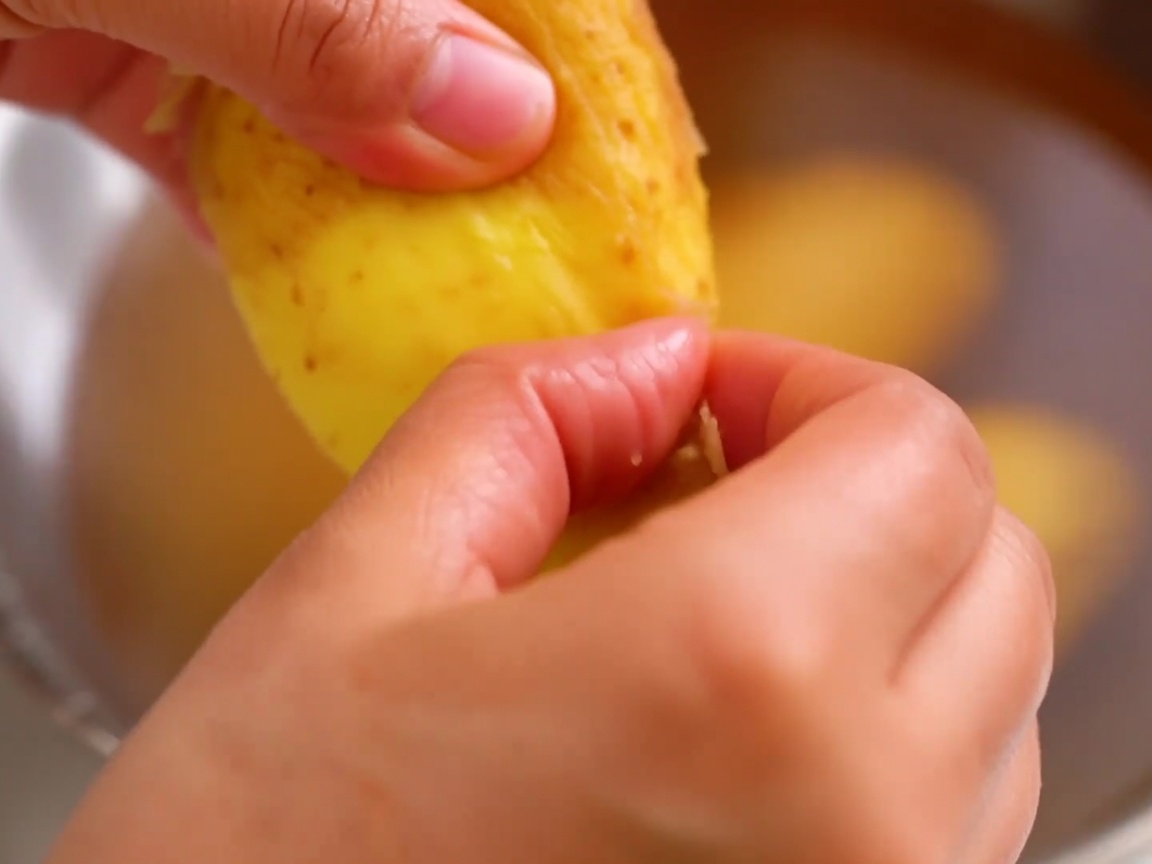 Épluchage de la peau dune pomme de terre décongelée avec les doigts.