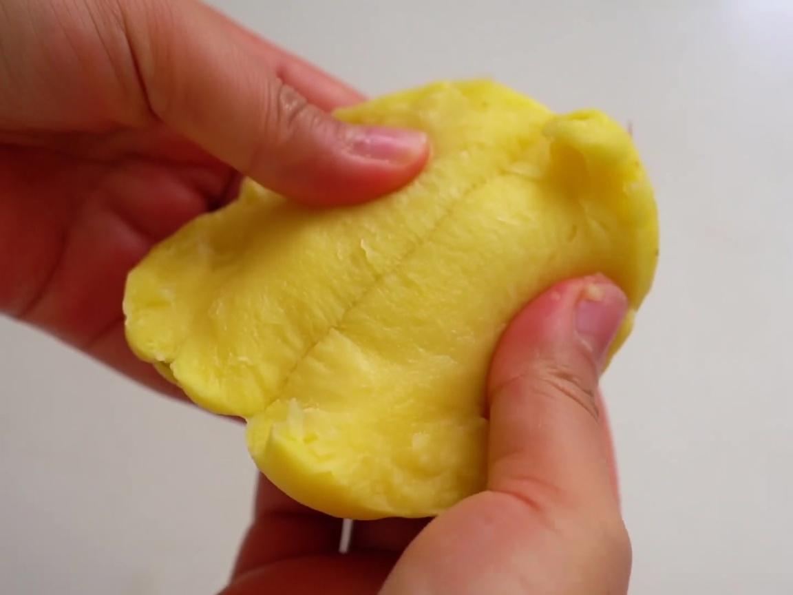 Des mains séparant une pomme de terre épluchée en deux moitiés grossières.